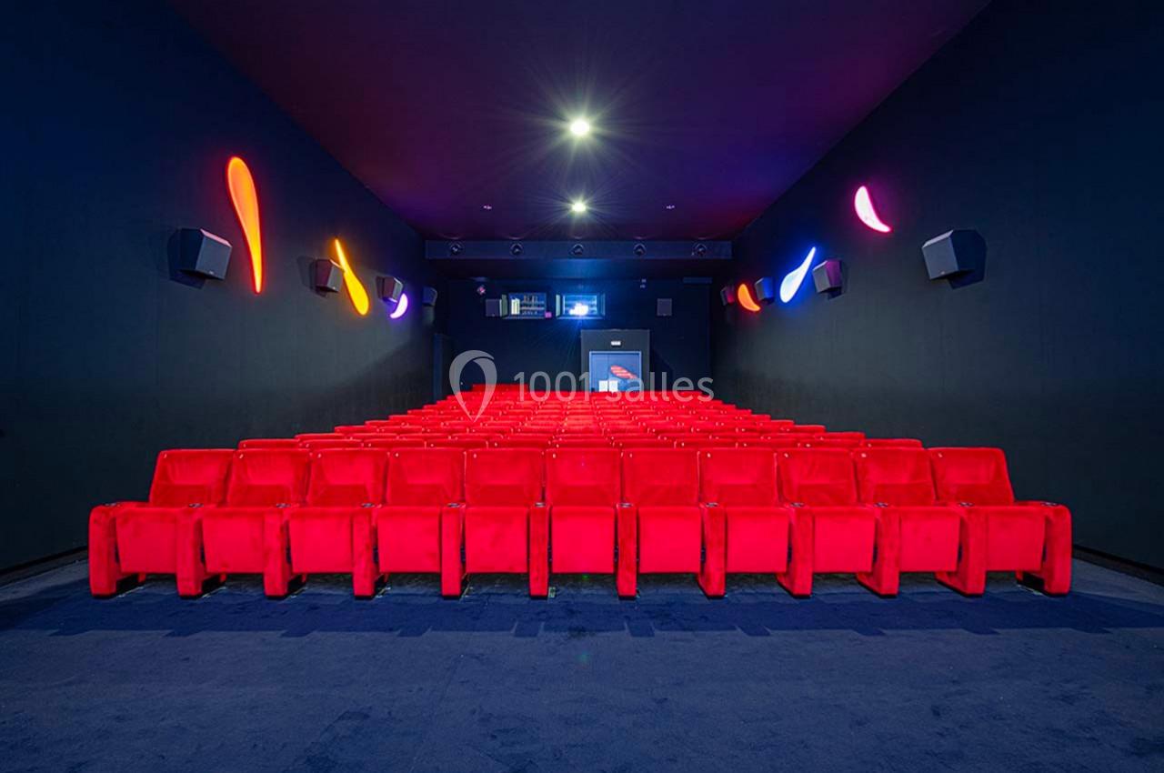 Salle de cinéma vide avec rangées de sièges rouges, murs sombres et éclairage coloré décoratif.