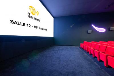 Salle lumineuse avec murs jaunes et gris, mobilier moderne espacé, grandes fenêtres laissant entrer la lumière naturelle.