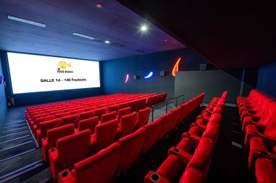 Salle lumineuse avec murs jaunes et gris, mobilier moderne espacé, grandes fenêtres laissant entrer la lumière naturelle.