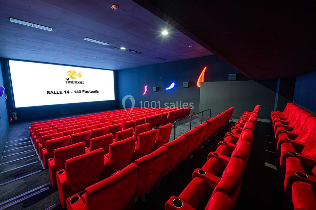 Salle de cinéma vide avec des sièges rouges alignés face à un grand écran affichant ’Salle 14 - 140 Fauteuils’.