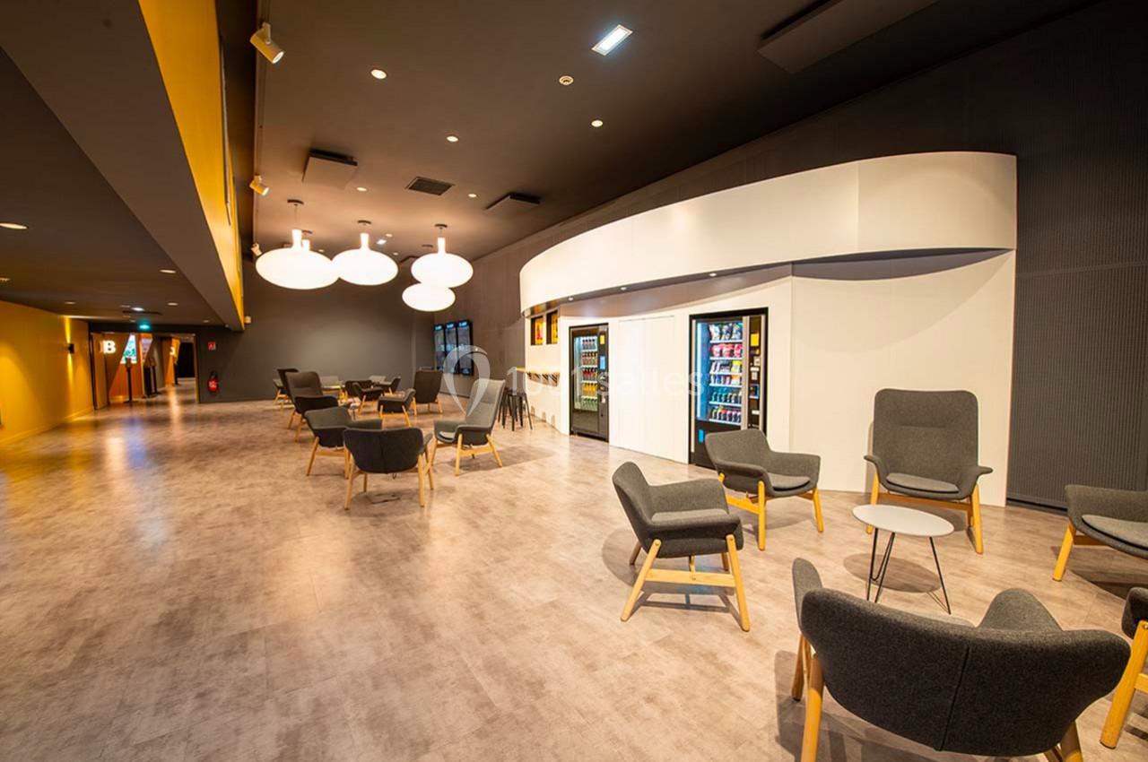 Espace intérieur moderne avec fauteuils, tables, distributeurs automatiques et éclairage suspendu.