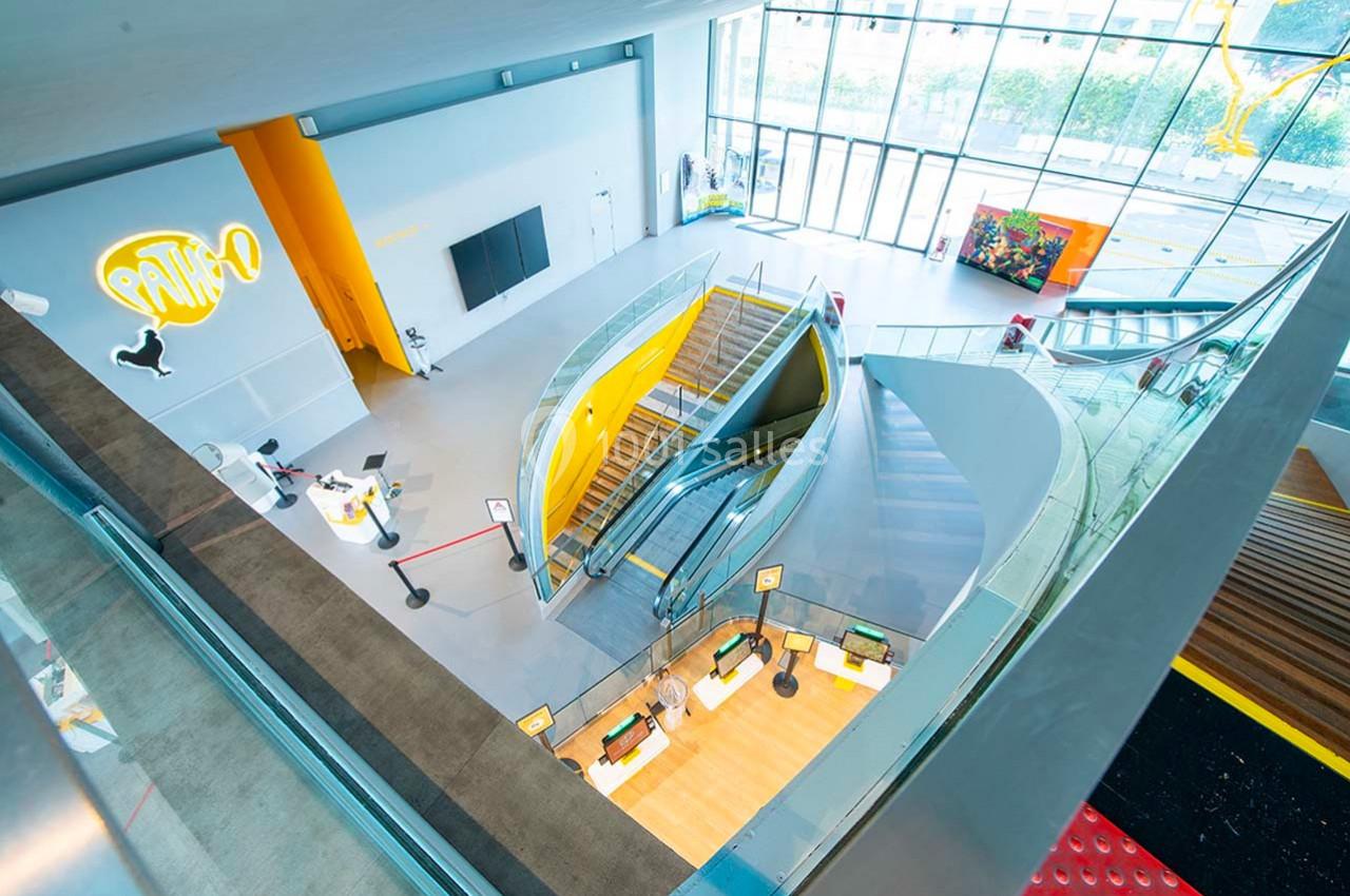 Vue intérieure d'un bâtiment moderne avec escalier central, espaces lumineux et éléments de design colorés.