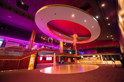 Salle de cinéma vide avec des rangées de fauteuils rouges et un éclairage tamisé.