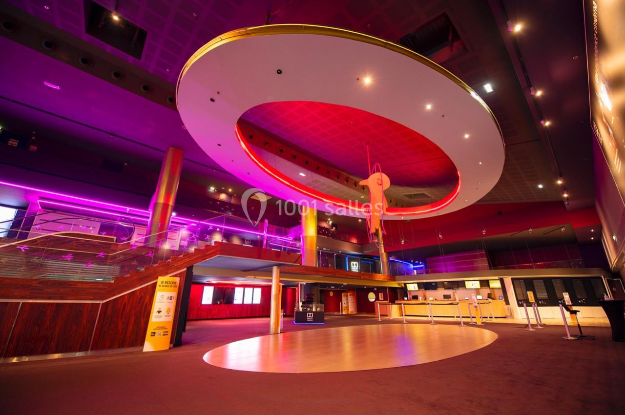 Intérieur d'un hall spacieux avec éclairage néon, escalier en bois et grande structure circulaire suspendue.