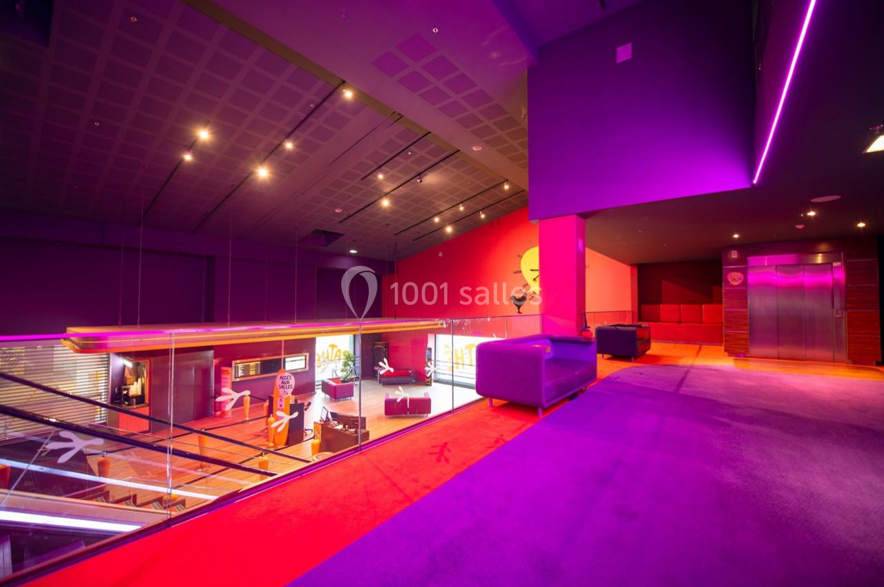 Intérieur moderne avec éclairage violet et rouge, canapé, ascenseur et vue sur un espace en mezzanine.