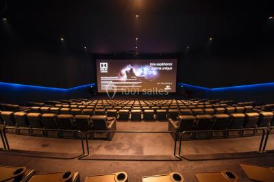 Salle de cinéma vide avec des rangées de fauteuils rouges et un éclairage tamisé.