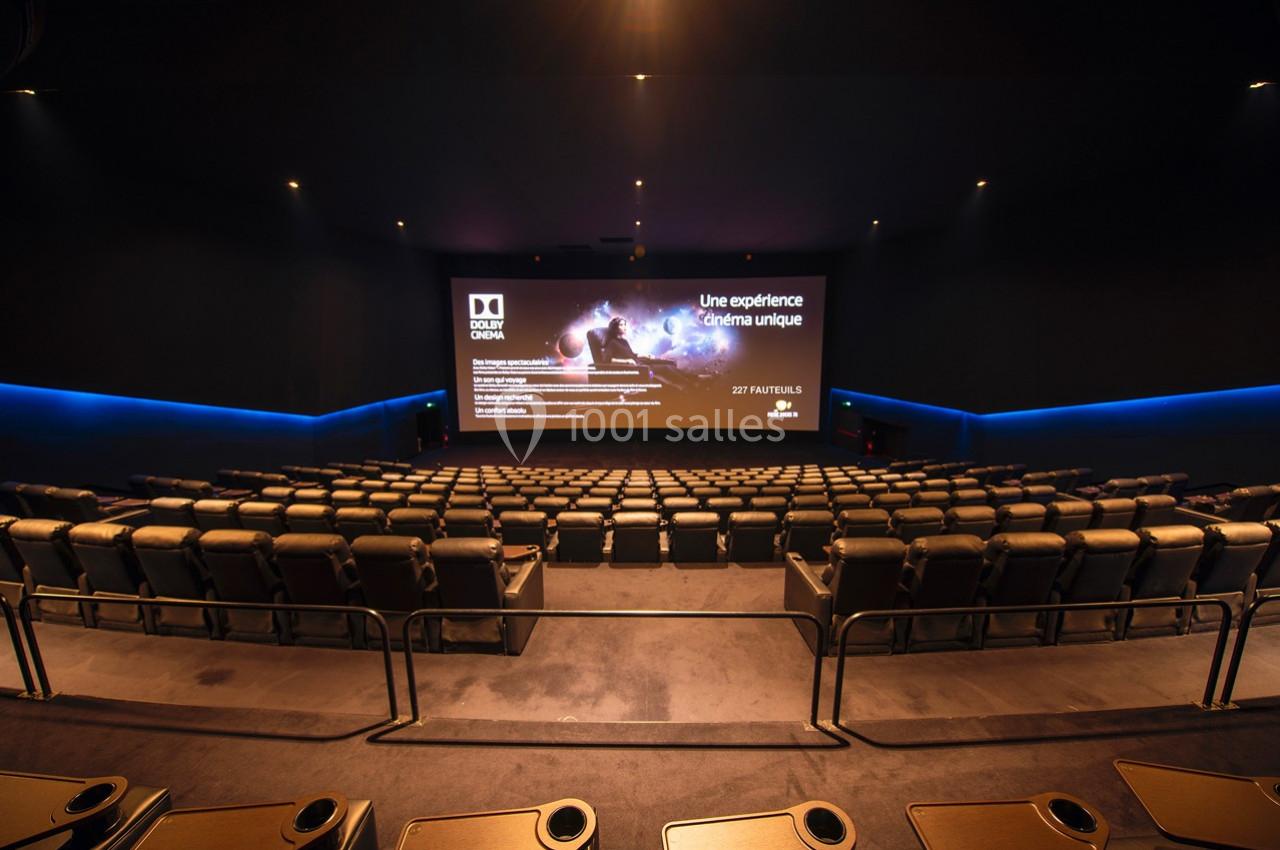 Salle de cinéma vide avec des sièges inclinables et un grand écran affichant une présentation promotionnelle.