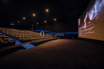 Salle de cinéma vide avec des rangées de fauteuils rouges et un éclairage tamisé.