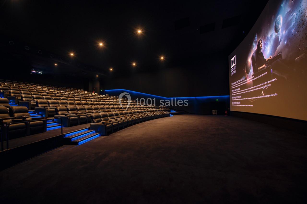 Salle de cinéma moderne avec sièges inclinés, éclairage tamisé et grand écran affichant une image spatiale.
