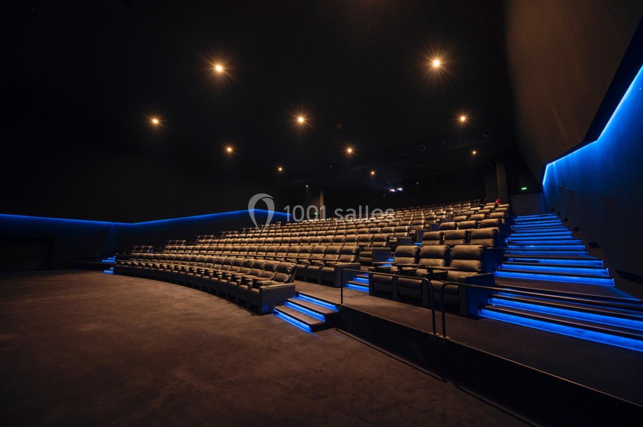 Salle de cinéma vide avec rangées de sièges en cuir et éclairage bleu le long des allées.