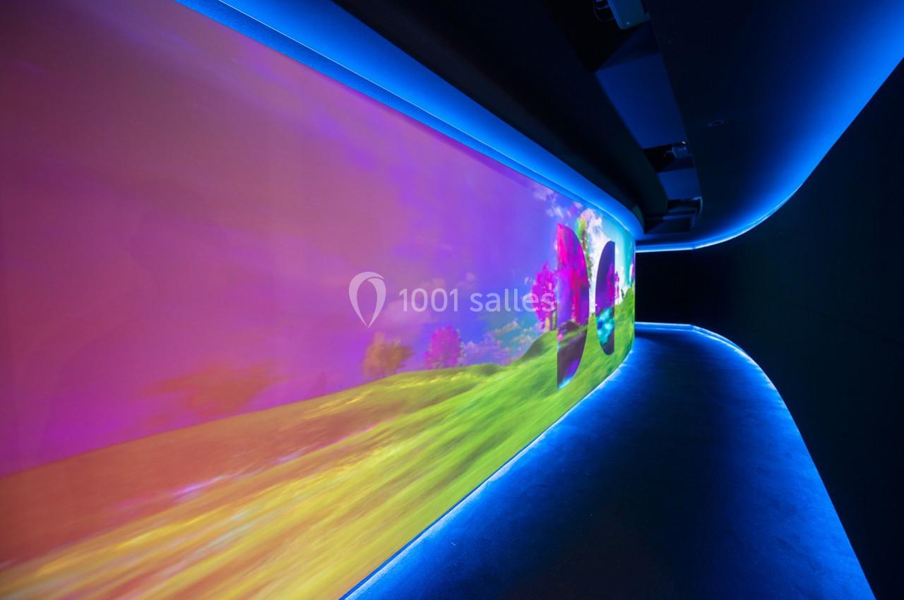 Projection colorée d'un paysage lumineux avec des arbres roses sur un mur incurvé dans un espace sombre.