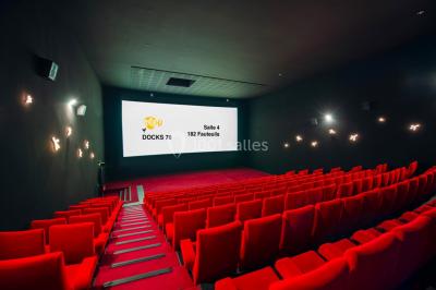 Salle de cinéma vide avec des rangées de fauteuils rouges et un éclairage tamisé.