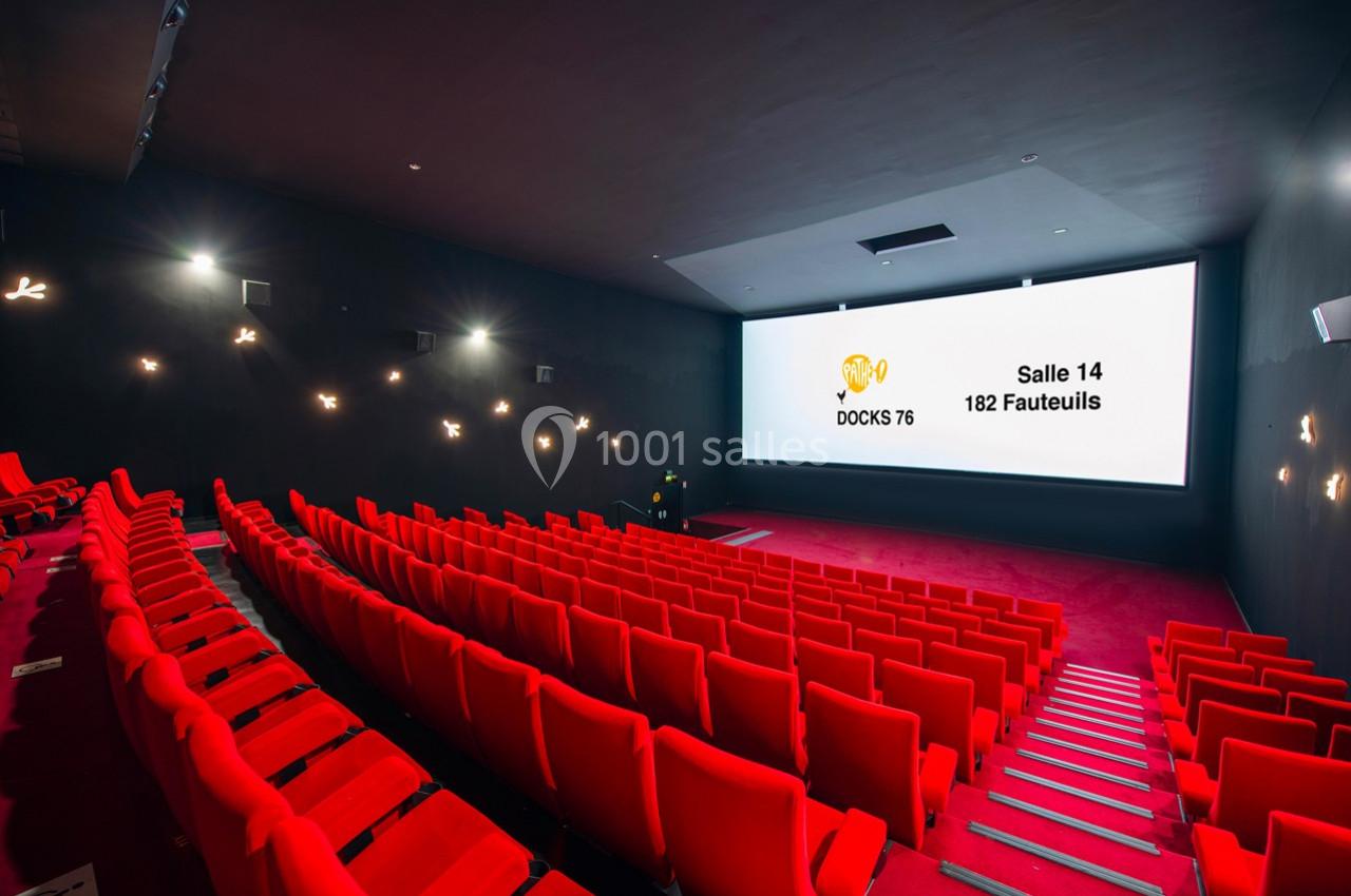 Salle de cinéma moderne avec sièges rouges alignés et grand écran affichant des informations sur la salle.