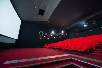 Salle de cinéma vide avec des rangées de fauteuils rouges et un éclairage tamisé.