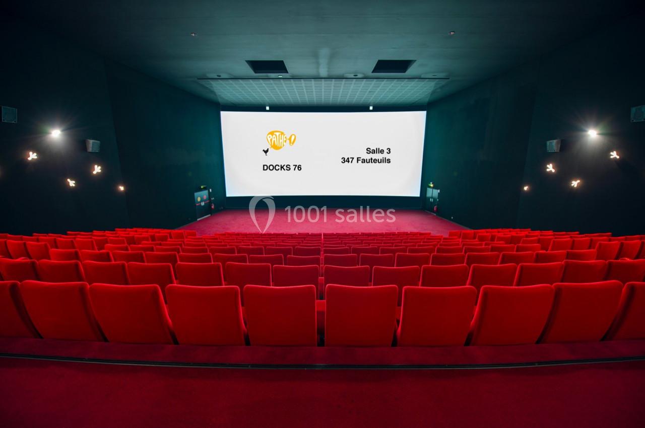 Salle de cinéma vide avec des rangées de fauteuils rouges et un écran affichant des informations sur la salle.