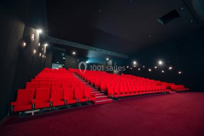 Salle de cinéma vide avec des rangées de fauteuils rouges et un éclairage tamisé.