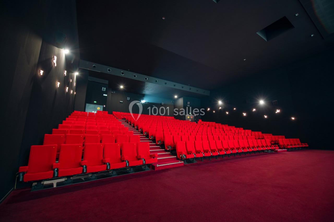 Salle de cinéma vide avec des rangées de fauteuils rouges et un éclairage tamisé.