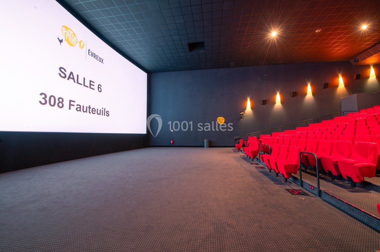 Salle de cinéma vide avec écran géant, rangées de fauteuils rouges et éclairage tamisé.