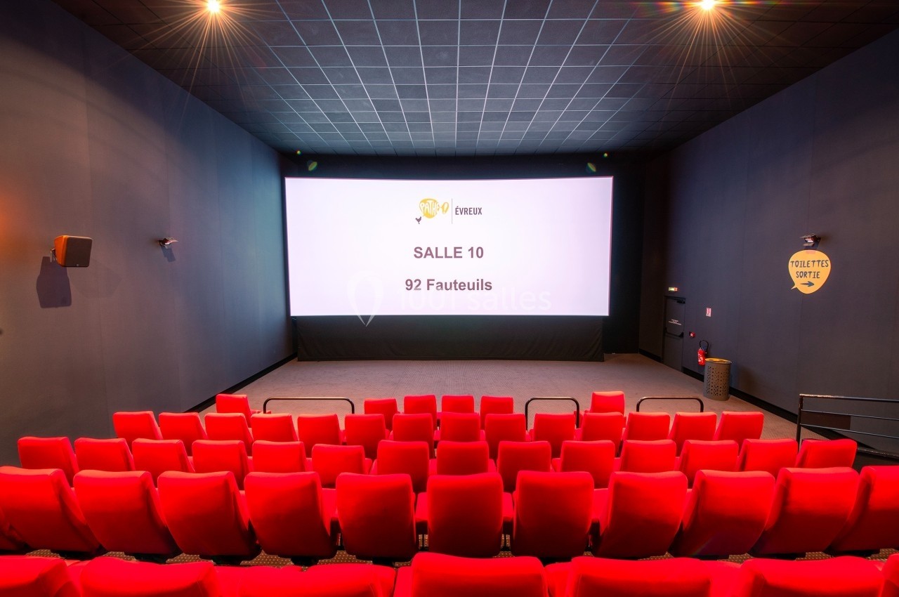 Salle de cinéma vide avec 92 fauteuils rouges, écran blanc affichant ’Salle 10’, éclairage tamisé.