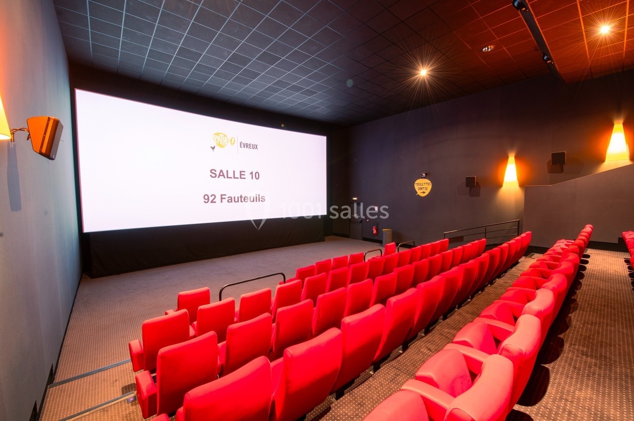 Salle de cinéma vide avec des rangées de fauteuils rouges, écran géant affichant ’Salle 10, 92 fauteuils’.