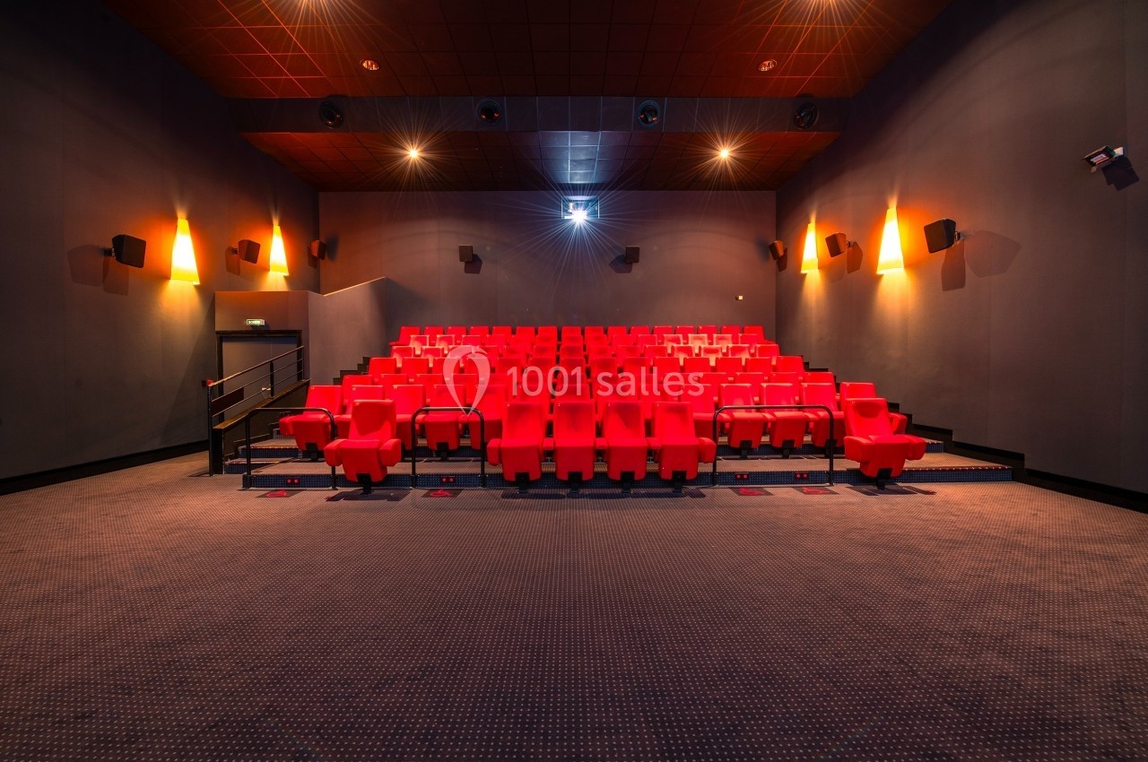 Salle de cinéma vide avec des rangées de sièges rouges et un écran éteint au fond.