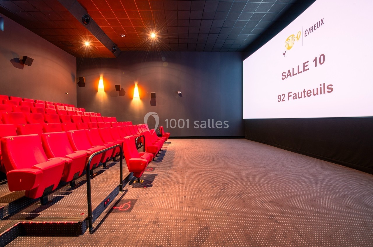 Salle de cinéma moderne avec rangées de fauteuils rouges et écran affichant ’Salle 10, 92 fauteuils’.
