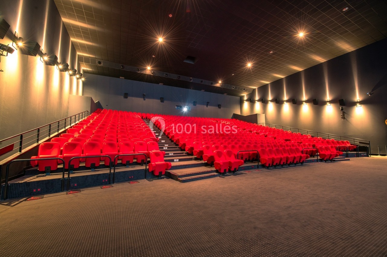 Salle de cinéma vide avec des rangées de sièges rouges et un éclairage tamisé au plafond.