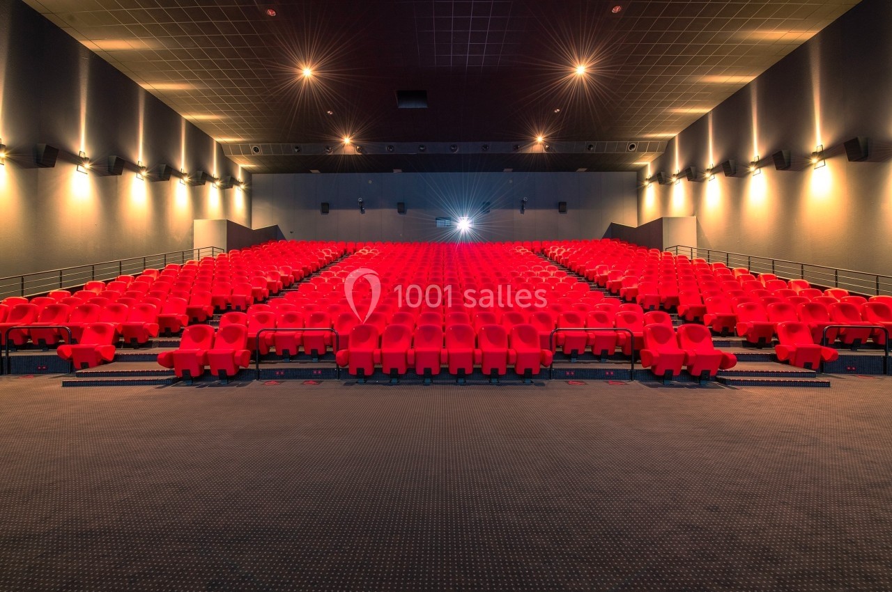 Salle de cinéma vide avec des rangées de sièges rouges et un écran illuminé en arrière-plan.