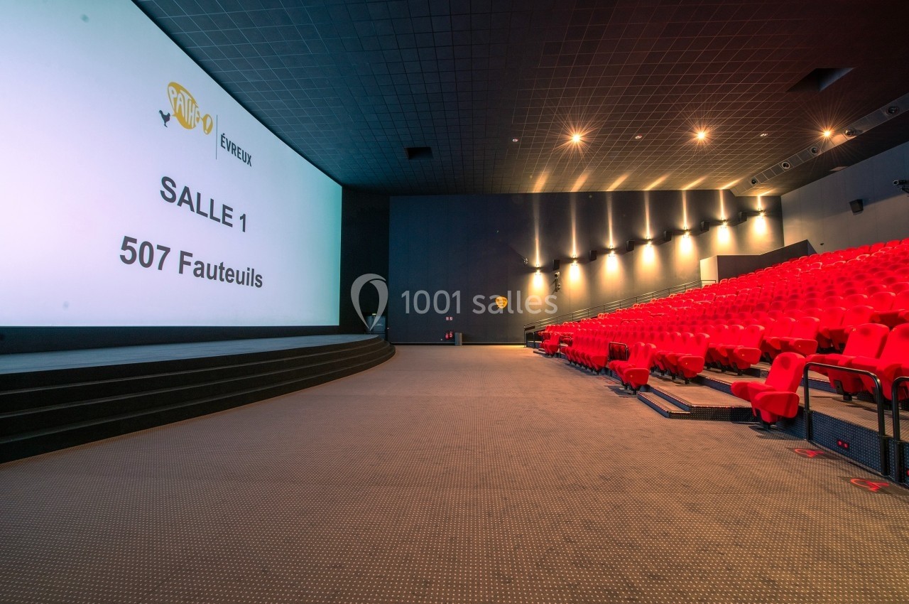 Salle de cinéma avec écran géant, rangées de fauteuils rouges et éclairage tamisé.