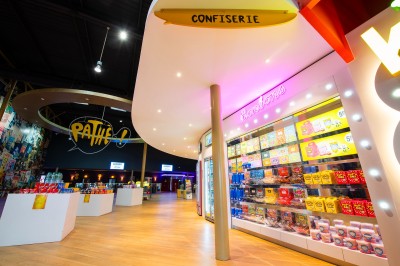 Entrée d'un cinéma Pathé avec affiches de films, sol violet, comptoirs de snacks et accès aux salles.