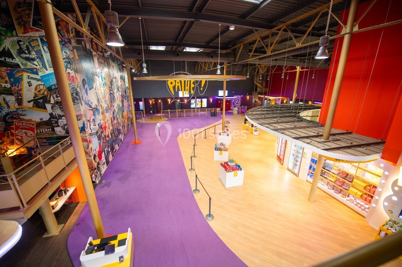 Vue intérieure d'un cinéma avec un sol violet, un mur décoré d'affiches et un espace de confiserie éclairé.