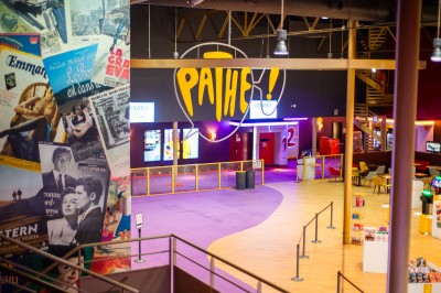 Entrée d'un cinéma Pathé avec affiches de films, sol violet, comptoirs de snacks et accès aux salles.