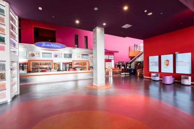 Salle de cinéma vide avec des rangées de sièges rouges et un éclairage mural coloré.
