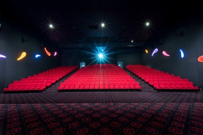 Salle de cinéma vide avec des rangées de sièges rouges et un éclairage mural coloré.