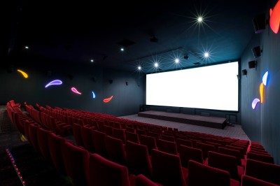 Salle de cinéma vide avec des rangées de sièges rouges et un éclairage mural coloré.