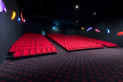 Salle de cinéma vide avec des rangées de sièges rouges et un éclairage mural coloré.