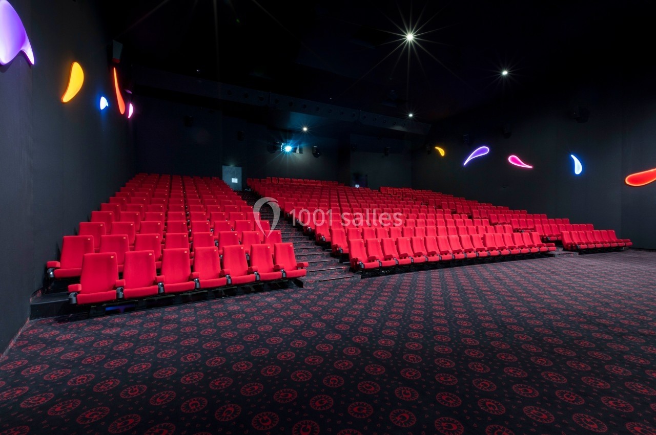 Salle de cinéma vide avec des rangées de sièges rouges et un éclairage mural coloré.