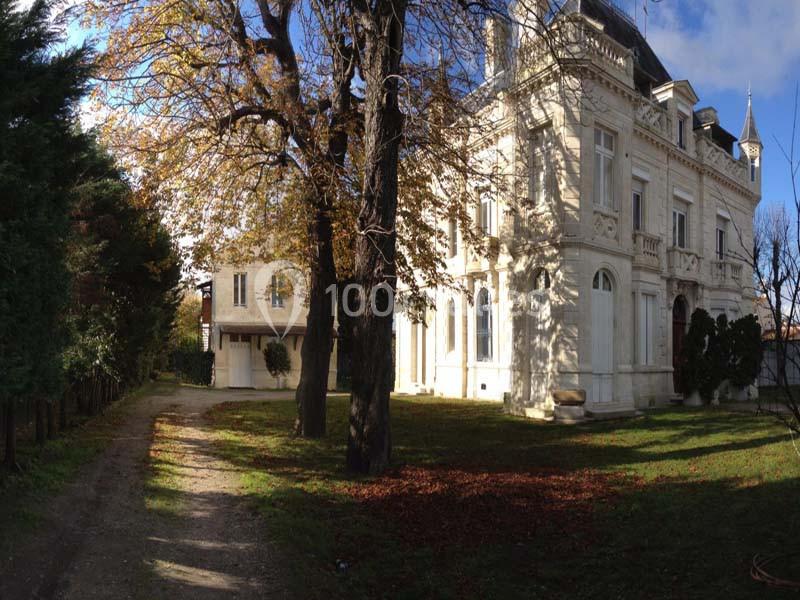 Façade d'un grand bâtiment ancien en pierre blanche, entouré d'arbres et d'une allée ombragée.