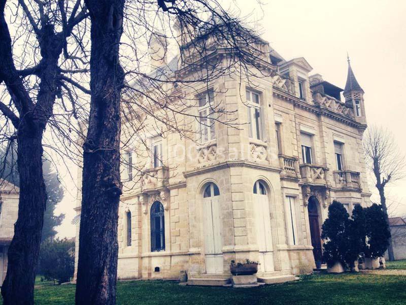 Manoir en pierre de style classique entouré d'arbres dénudés en hiver, avec un jardin verdoyant au premier plan.