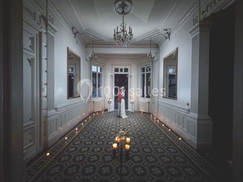 Un couple se tient au centre d'une pièce élégante éclairée par des bougies, avec des miroirs et un sol à motifs.