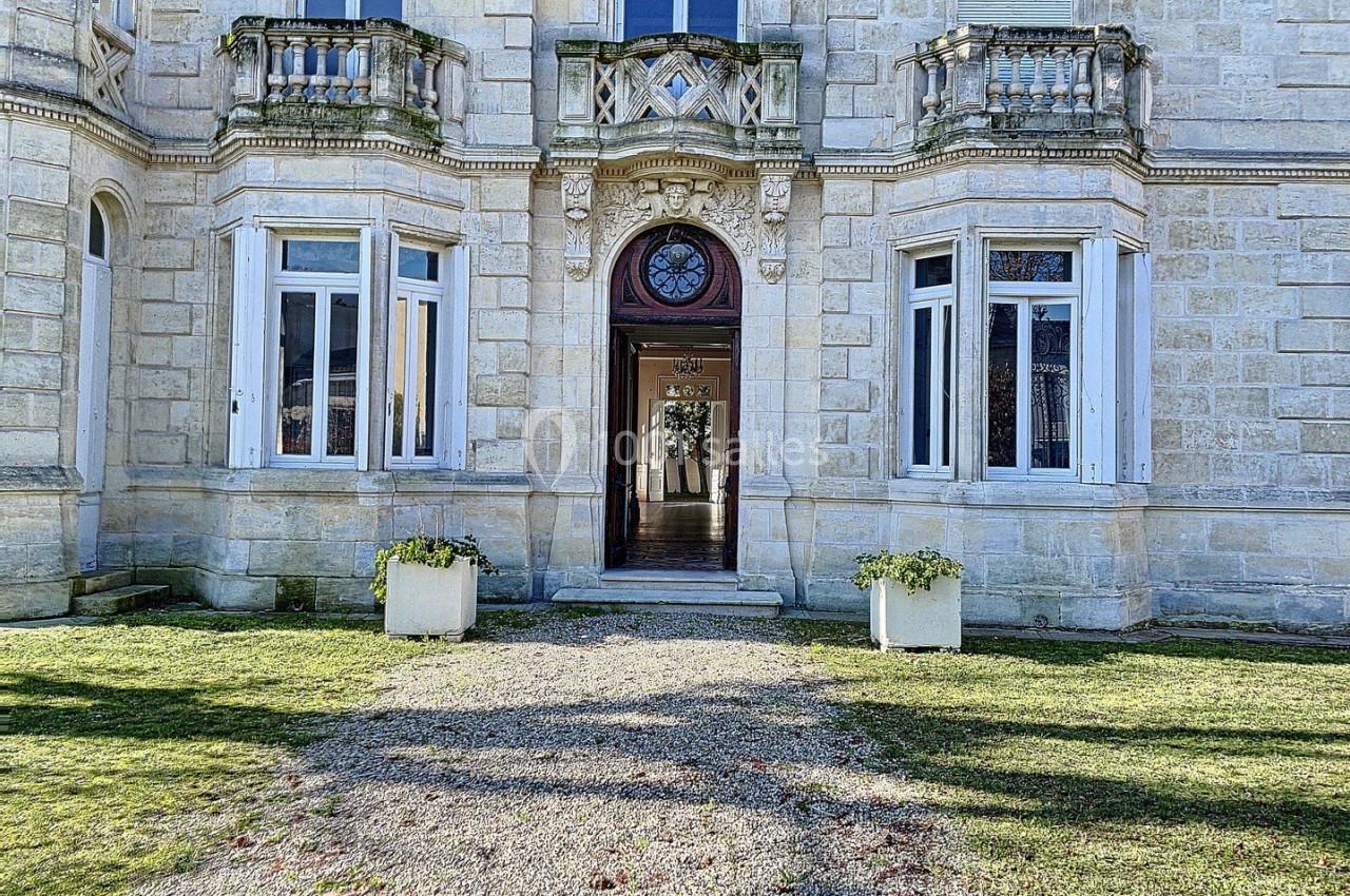 Façade d'un bâtiment en pierre avec une porte centrale ornée et des fenêtres symétriques, entourée d'un jardin.