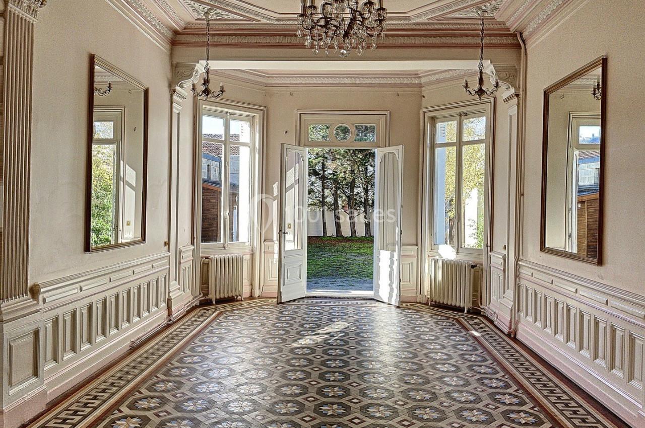 Salle lumineuse avec carrelage géométrique, moulures au plafond, miroirs muraux et portes ouvertes sur un jardin.
