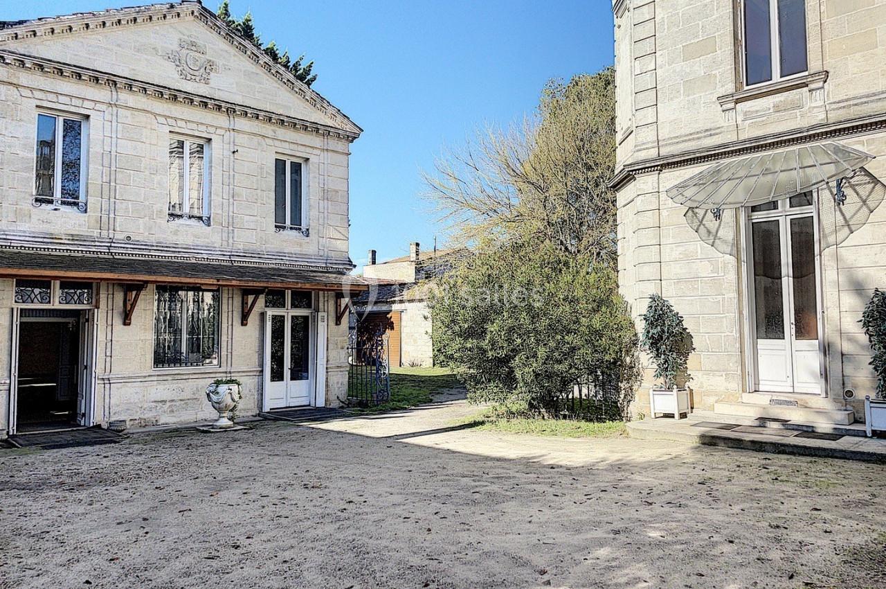 Cour extérieure avec bâtiments en pierre, grandes fenêtres et arbres en arrière-plan sous un ciel dégagé.
