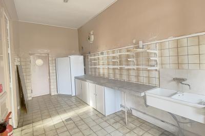 Cuisine vide avec carrelage beige, évier mural, étagères blanches, réfrigérateur et porte au fond.