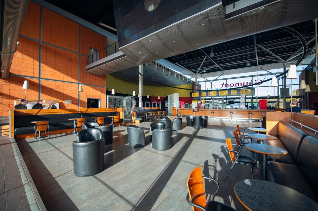 Espace intérieur lumineux avec tables, chaises et fauteuils, dans un lieu public moderne avec un comptoir au fond.