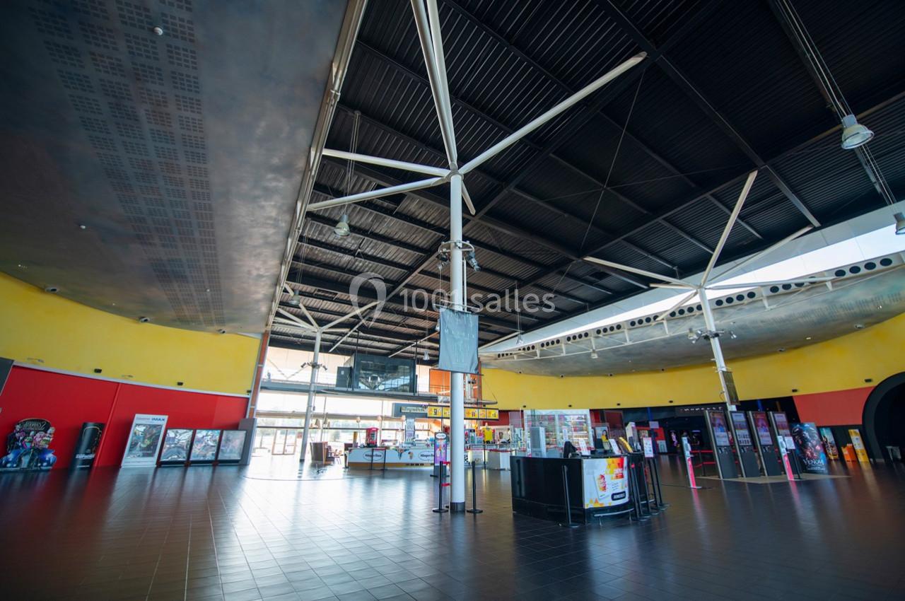 Intérieur spacieux d'un bâtiment avec plafond métallique, murs colorés et bornes de jeux alignées.