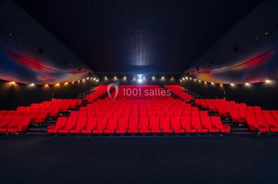 Salle de cinéma vide avec fauteuils rouges, grand écran allumé et plafond illuminé par des motifs lumineux.