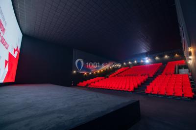 Salle de cinéma vide avec fauteuils rouges, grand écran allumé et plafond illuminé par des motifs lumineux.