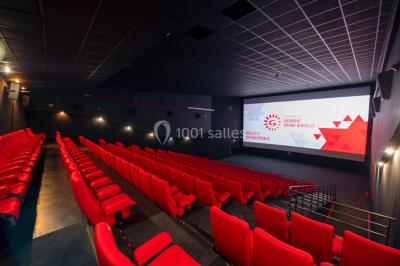 Salle de cinéma vide avec fauteuils rouges, grand écran allumé et plafond illuminé par des motifs lumineux.