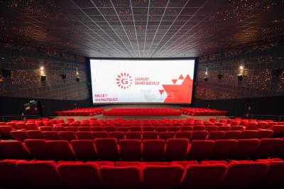 Salle de cinéma vide avec fauteuils rouges, grand écran allumé et plafond illuminé par des motifs lumineux.